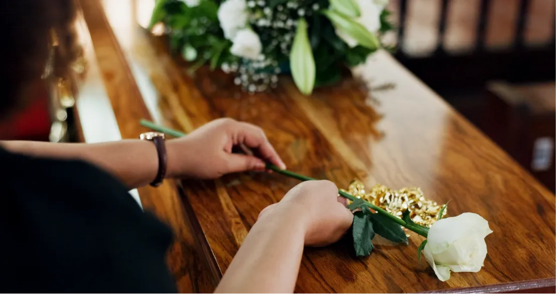 Woman placing a white rose on a wooden coffin, representing funeral planning and final expense insurance - Senior Life Insurance